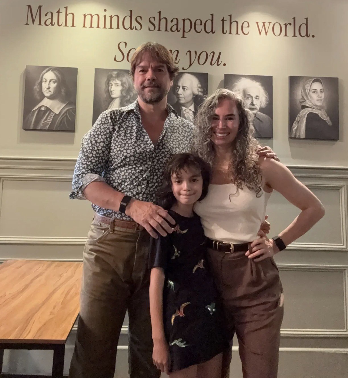 Marcelo Ambrozio, Violetta, and Vivianne Wright at SOMATH — School of Math on the Upper West Side of Manhattan, under the classroom's 'Math minds shaped the world' portrait wall of Fermat, Newton, Euler, Einstein, and Maryam Mirzakhani. Vivianne and Violetta were featured in the New York Post's September 9, 2026 article on the rise of NYC homeschooling.